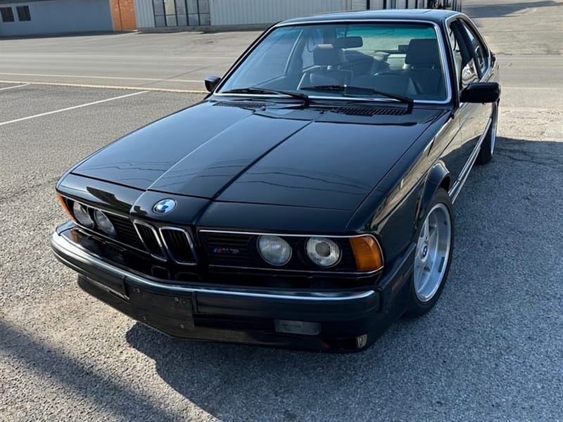 Black 1988 BMW M6 coupe photographed at a front three-quarter angle on the lot in front of the shop