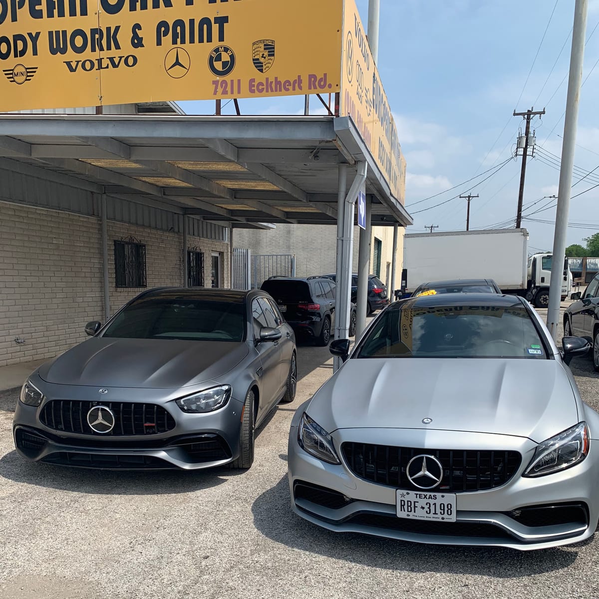 The European Car Parts shop sign listing MINI, Volvo, Mercedes-Benz, BMW and Porsche with the address 7211 Eckhert Rd., and two Mercedes-Benz cars parked under the front canopy